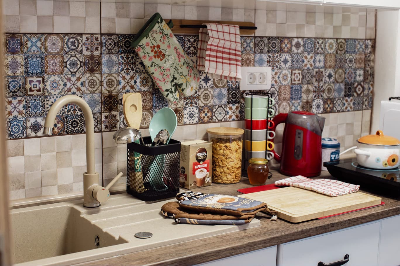 A kitchen featuring a sink, countertop, and a tiled wall, showcasing a clean and organized cooking space.
